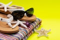 Women`s Beach Flip Flops, Colorful Striped Beach Towels and black Sunglasses decorated with Starfish on yellow background Royalty Free Stock Photo