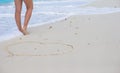 Women's beautiful smooth legs standing near big heart on white sand beach Royalty Free Stock Photo