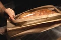 Women's caring hands pack fresh artisan bread in a paper bag with a transparent insert. Craft bread packaging