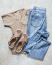 Women`s casual walking wear - comfortable leather sandals, beige t-shirt and blue jeans on a light background, top view
