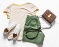 Women`s cotton green bermuda shorts, yellow t-shirt, crossbody bag, white leather sneakers on a light background, top view. Royalty Free Stock Photo