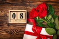 Women`s day background. 8 march wooden calendar, red roses, gift with red ribbon on the wooden background. Copy space, flat lay