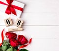 Women`s day background. 8 march wooden calendar, red roses, gift with red ribbon on the white wooden background. Copy space, flat