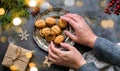 Women& x27;s elegant hands touch a plate of cookies-nuts on a dark table. Framed layout of Christmas decorations, gifts, nuts