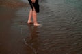 Women`s feet on the beach in the water go on a wet stove with shells