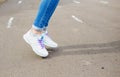 Women`s feet in blue jeans and white sneakers on the asphalt. close up Royalty Free Stock Photo