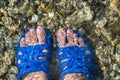 Women`s feet feet and fingers in blue rubber flip-flops, Slippers, are submerged in salty sea water near the shore