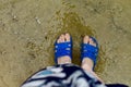 Women`s feet feet and fingers in blue rubber flip-flops, Slippers, are submerged in salty sea water near the shore, on smooth ston