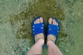 Women`s feet feet and fingers in blue rubber flip-flops, Slippers, are submerged in salty sea water near the shore, on smooth ston