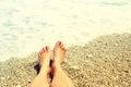 Women`s feet on a pebble beach against the background of sea foam in summer. Beach holidays, holidays, vacation Royalty Free Stock Photo