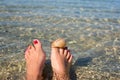 Women`s feet with a pedicure, which are immersed in the water on the beach. There is a starfish and a shell on the big toes