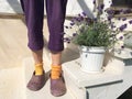 Women`s feet in purple knitted trousers, socks of different colors yellow and orange and dirty purple galoshes on a white woode