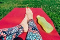 Women`s feet with red nails on pink yoga Mat on grass and green