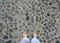 Women`s feet with red pedicure shoes in white sandals stand on the pavement. Top view Royalty Free Stock Photo