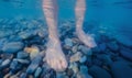 Women's feet stand on a pebble bottom in seawater. Underwater photo. Royalty Free Stock Photo