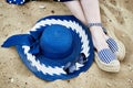 Women`s feet in striped sandals, blue hat and sunglasses on the sand Royalty Free Stock Photo