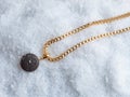 Women`s golden chain and pendant with round black volcanic lava stone on white snow background Royalty Free Stock Photo