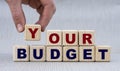 Women`s hand folds wooden cubes with the words YOUR BUDGET on a gray background