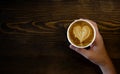 Women`s Hand holding cup of cappuccino coffee with heart shape latte art on old wood table Background, Latte coffee on old wooden Royalty Free Stock Photo