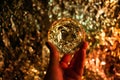 Women`s hand holding a fortune teller crystal ball and looking into the future. Blurred sparkly light background