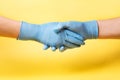 Women hands in blue medical gloves on a yellow background Handshake Coronovirus concept