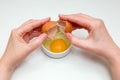 Women`s hands breaking a raw egg into a white cup standing on a white background Royalty Free Stock Photo