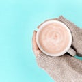 Women`s hands with cup of coffee above trend color blue paper surface. Sweet hot fragrant Cappuccino close up