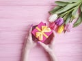 Women`s hands hold anniversary a gift box holiday march birthday, present a bouquet of tulips on a pink wooden background Royalty Free Stock Photo