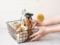 Women`s hands hold black metal basket with eco-friendly kitchen set. Food, brushes, wood appliances, bags, bottle and jar