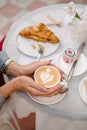 Women's hands hold a cup of coffee. A cut croissant lies on a table nearby against a blurred background. Royalty Free Stock Photo