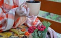 Women`s hands hold a cup of hot drink, Autumn, fall leaves, hot steaming cup of coffee and a warm scarf on wooden table