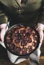 Women`s hands hold a freshly baked traditional plum cake in a baking dish over a wooden table
