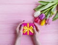 Women`s hands hold anniversary beauty a gift box holiday march birthday, present a bouquet of tulips on a pink wooden background Royalty Free Stock Photo