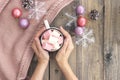 Women`s hands holding cup with hot coffee with foam and marshmallows on of wooden table.The concept of winter, warmth, holidays