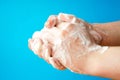 Women`s hands are holding soap. Soap foam on the hands. Yellow soap in the hands. Woman washes soap with hands side view on a blu