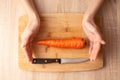 Women`s hands, knife and carrot on the wooden cutting board