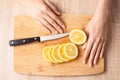 Women`s hands, knife and sliced lemon on the wooden cutting board
