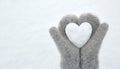 Women`s hands in light gray knitted mittens hold a beautiful white heart made of snow Royalty Free Stock Photo