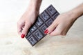 Women`s hands with a manicure hold a whole bar of chocolate. Wooden background. Chocolate Day.