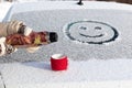 Women`s hands in mittens pour boiling water into a mug from a thermos on a snowy car trunk on a sunny winter day. Smiley drawing