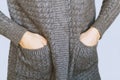 Women`s hands in the pockets of a warm gray cardigan against a gray wall. A young girl put her hands in a knitted sweater to keep