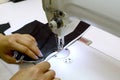 Women`s hands sew a black satin fabric, stitching a white satin on a sewing machine.