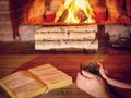 Women`s hands warm up on a hot cup of tea near a burning fireplace, an open book is on the table Royalty Free Stock Photo