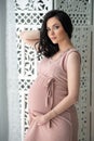 Women`s health and pregnancy. A beautiful pregnant woman in a tender pink dress is standing near an openwork wooden