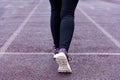 Women`s legs in black sports leggings and sports shoes on a treadmill of a sports open stadium