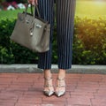 Women`s legs in grey high heels shoes. Bright grey shoes, bag and blue pants. Cotton pants, stylish ladies shoes and bag. Business