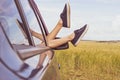 Women`s legs in shabby blue sneakers stick out of the car window Royalty Free Stock Photo