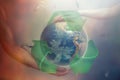 Woman`s and man`s hands support the globe of planet Earth with sign of recycle. Around the flying plastic debris. The concept of
