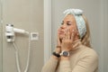 Women's morning preparations for work. A girl applies cream to her face in front of a mirror in the bathroom