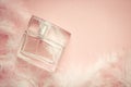 Women`s perfume on a delicate pink background with feathers
